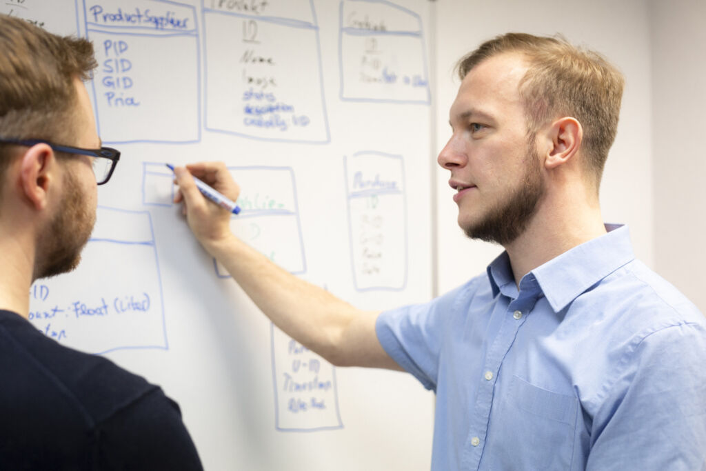 Mitarbeiter erklärt jemandem unseren Bereich SAP-Anwendung am Whiteboard