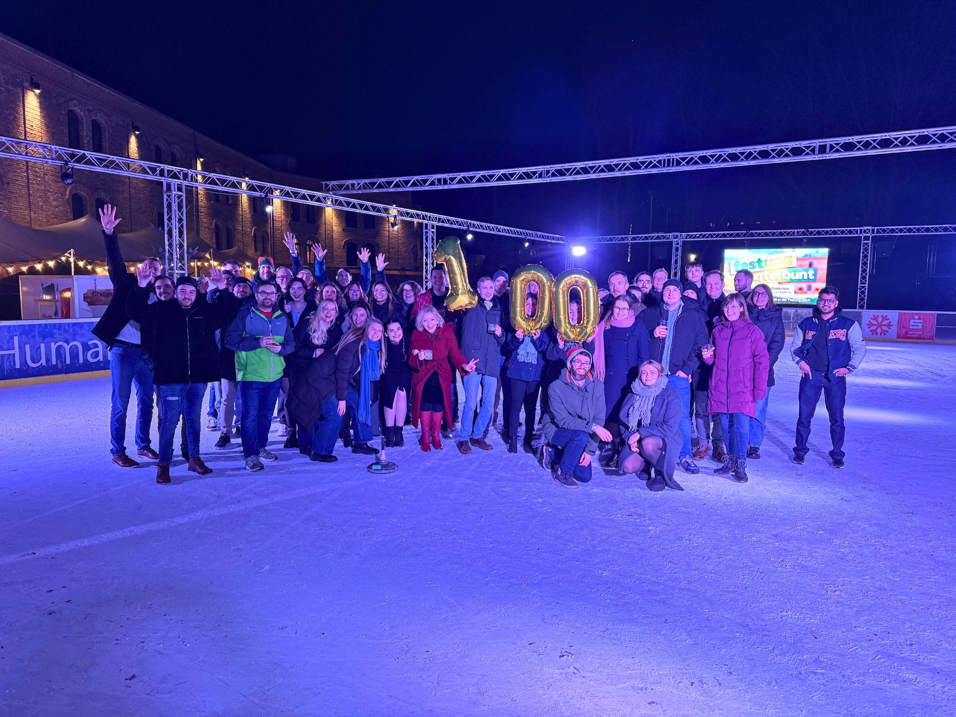 100 Mitarbeitende in einer Schneelandschaft, mit einem Luftballon mit der Zahl 100